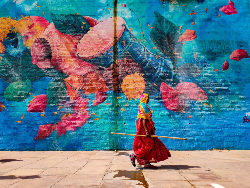 Woman in colourful clothing walking past a painted mural in India